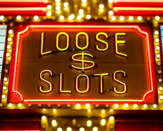 Bright neon lights display the words 'Loose Slots' with a dollar sign in the center. The sign is outlined with bulbs, creating a vibrant and flashy effect typical of a casino or entertainment venue.